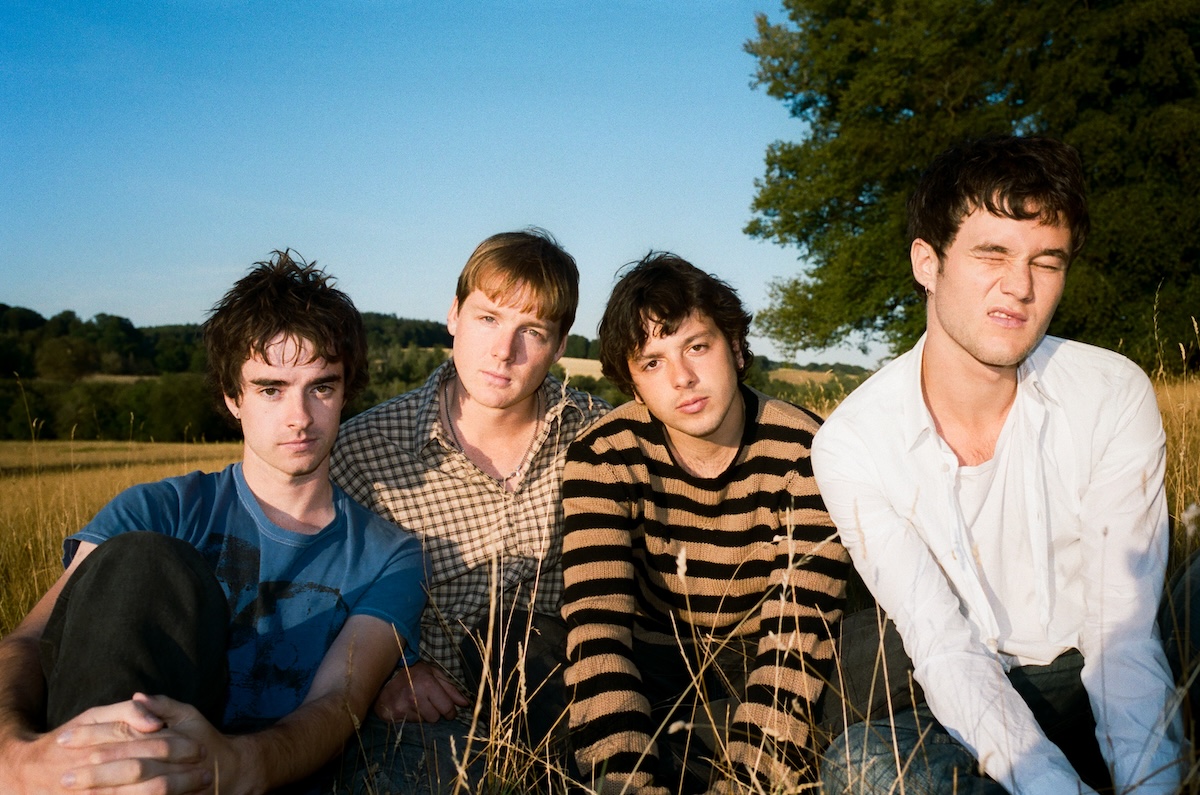 Outdoor promo photo of post-punk band Radio Free Alice sitting together in a grassy field under a clear blue sky.